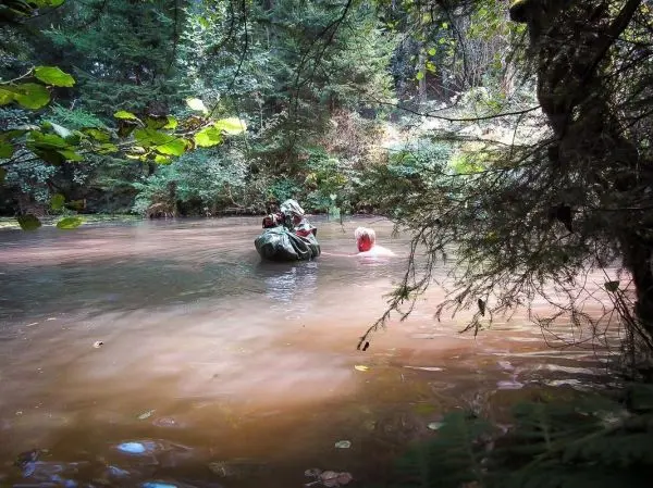 Person paddelt in einem trüben Gewässer zwischen Bäumen und Sträuchern