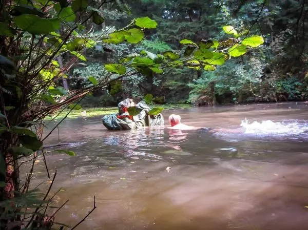Personen schwimmen in einem trüben Gewässer zwischen Pflanzen und Bäumen
