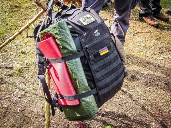 Schwarzer Rucksack mit grüner und roter Plane an einem Baum befestigt