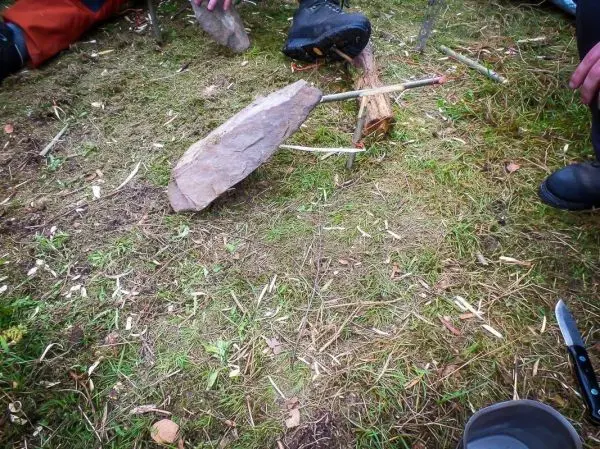 Stein liegt auf dem Boden neben Holzstücken und Werkzeugen beim Überlebenstraining