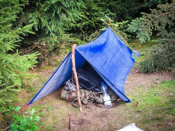 Tarp-Notunterkunft aus blauer Plane über einem Rucksack und Wasserflasche