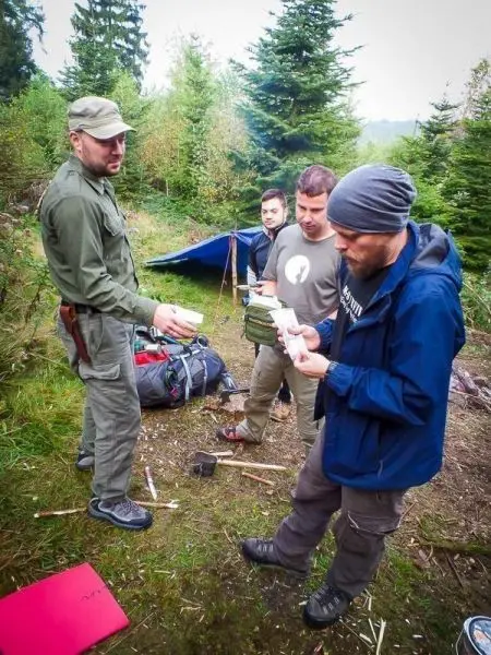 Vier Personen stehen um einen Rucksack, einer hält ein Blatt Papier in der Hand