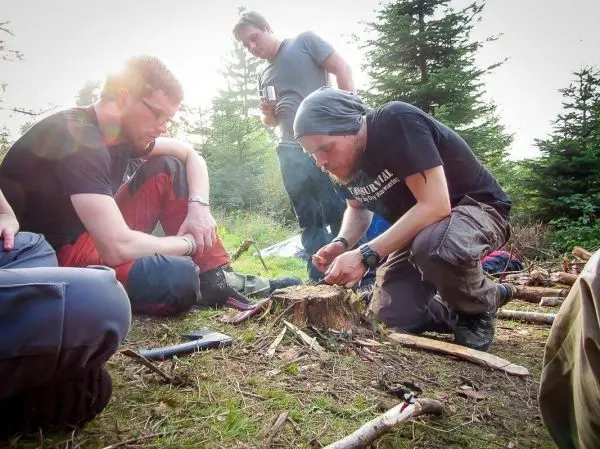 Zunder wird mit einem Messer bearbeitet, während zwei Personen aufmerksam zuschauen