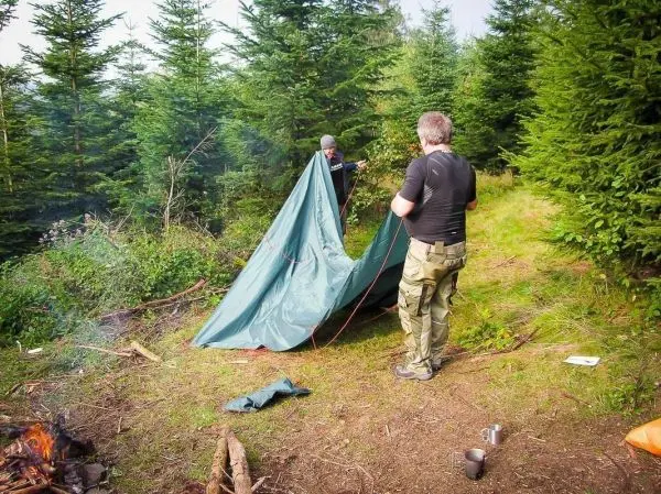 Zwei Personen bauen eine Tarp-Notunterkunft im Wald auf