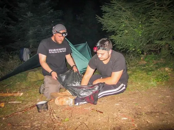 Zwei Personen bereiten eine improvisierte Trage aus einer Mülltüte vor