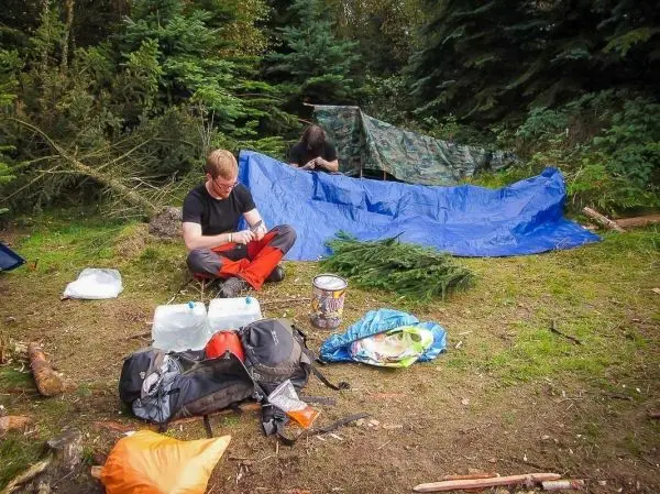 Zwei Personen bereiten eine Tarp-Notunterkunft mit einer blauen Plane vor