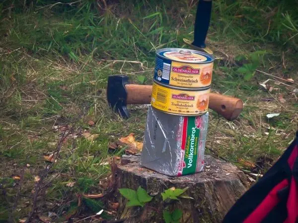 Dose auf Holzscheit mit Axt und weiteren Dosen darauf platziert