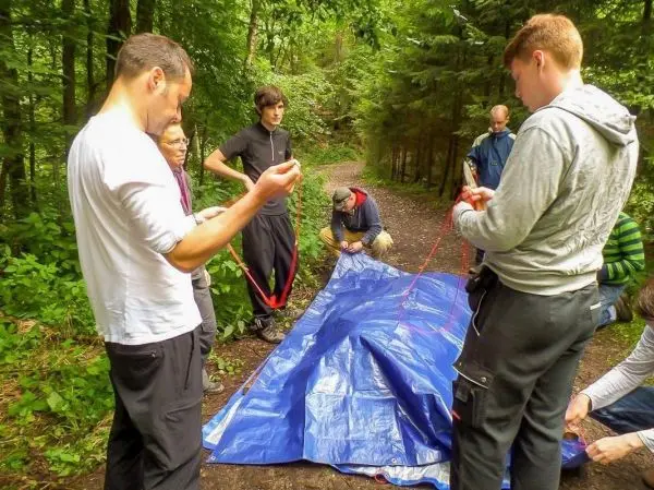 Gruppe arbeitet an einer blauen Plane im Wald beim Überlebenstraining