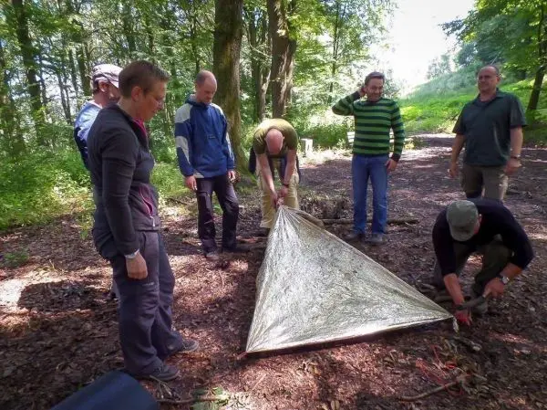 Gruppe baut Tarp-Notunterkunft im Wald auf, während einige Personen helfen