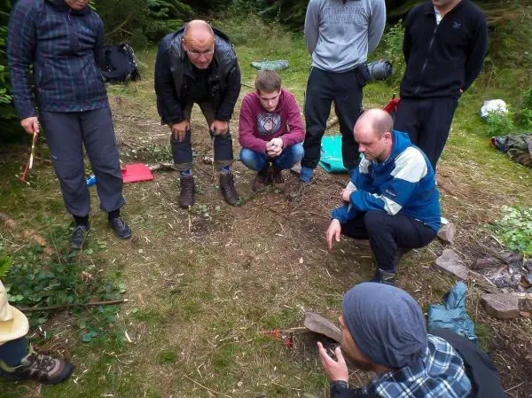 Gruppe beobachtet eine Feuerstelle im Wald, während jemand Anweisungen gibt