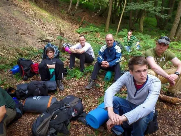Gruppe sitzt auf dem Boden im Wald, Rucksäcke und Isomatten liegen verstreut