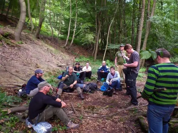Gruppe sitzt im Wald auf dem Boden und diskutiert über Ausrüstung