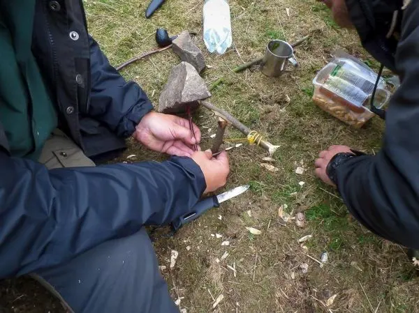 Hände binden einen Stock mit Schnur an einen anderen Stock zur Konstruktion