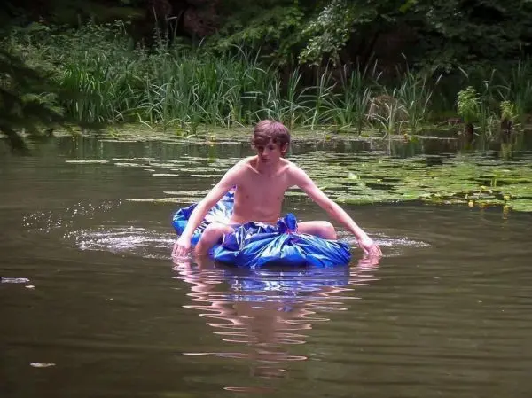 Junge paddelt auf einer blauen Luftmatratze in einem ruhigen Gewässer