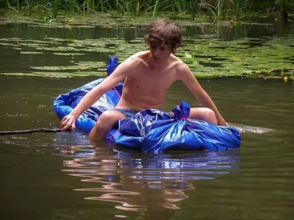 Junge sitzt auf improvisiertem Floß aus blauen Planen im Wasser