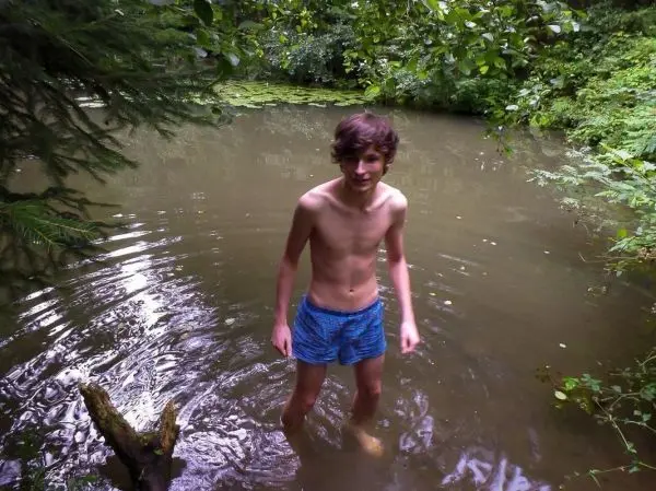 Junge steht im Wasser eines kleinen Teichs umgeben von Pflanzen