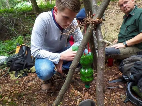 Junger Mann montiert eine Wasserfilterkonstruktion aus Plastikflaschen an einem Holzgestell