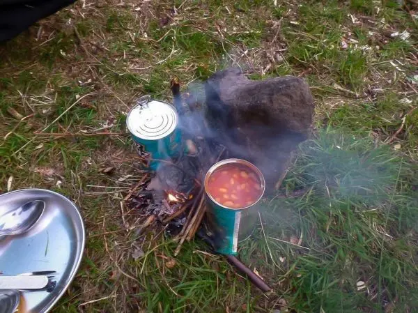 Kessel mit Bohnen über kleinem Feuer, Rauch steigt auf, daneben eine Dose
