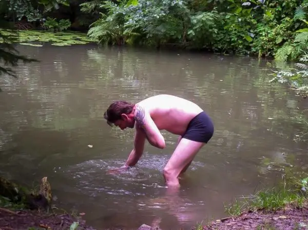Mann beugt sich über den Rand eines Gewässers und greift ins Wasser