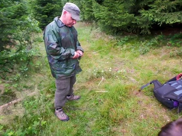 Mann in Tarnjacke hält einen Stock in der Hand, steht auf einer Wiese