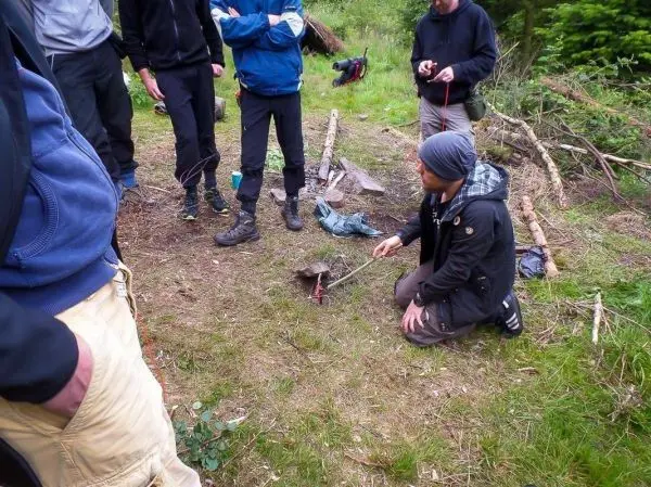 Mann kniet neben einem kleinen Feuer und hält einen Stock über die Flamme