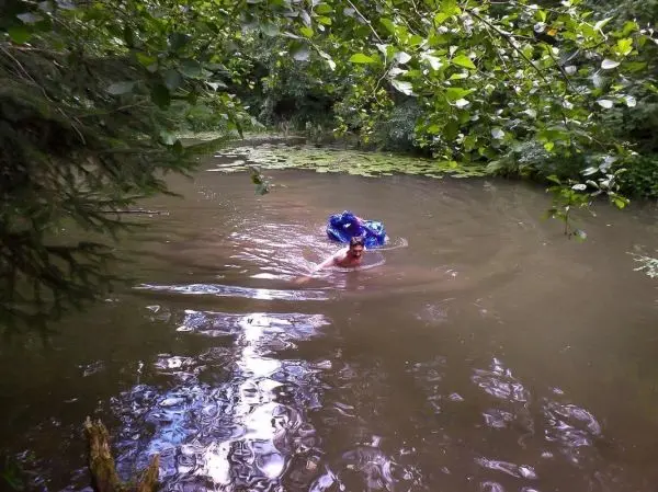 Mann schwimmt in einem trüben Gewässer unter Bäumen mit Wasserpflanzen