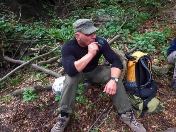 Mann sitzt auf dem Boden und raucht eine Pfeife, Rucksack neben ihm