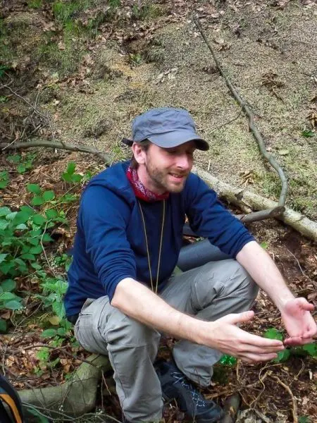Mann sitzt im Wald und gestikuliert mit den Händen