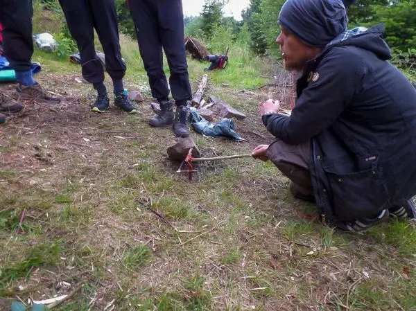 Mann sitzt neben einem Stock mit aufgespießtem Fleisch über einem kleinen Feuer