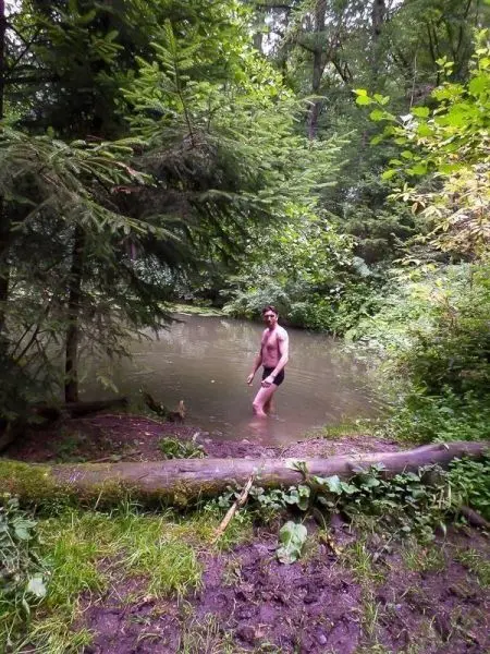 Mann steht im Wasser eines kleinen Teichs, umgeben von Bäumen und Pflanzen