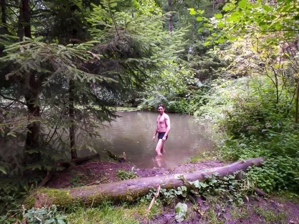 Mann steht im Wasser eines kleinen Teichs, umgeben von Bäumen und Pflanzen