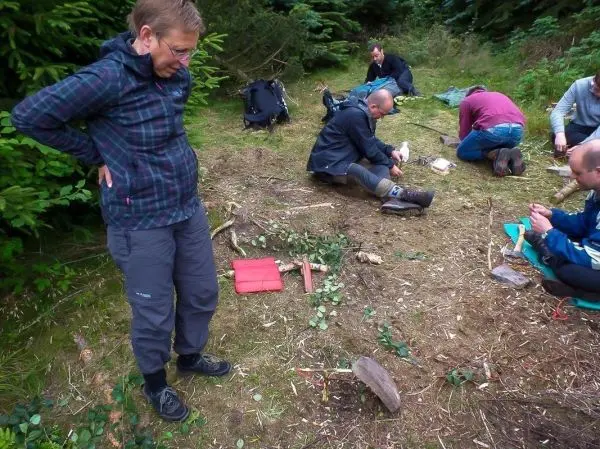 Mann steht neben einer selbstgebauten Schlagfalle auf dem Boden, andere arbeiten an Holzstücken