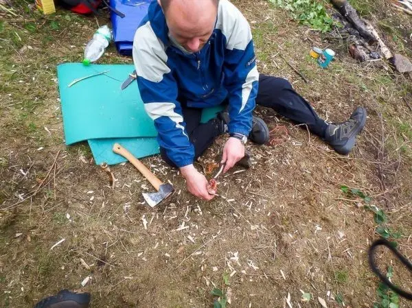 Messer und Axt liegen neben einem Mann, der Holzspäne bearbeitet