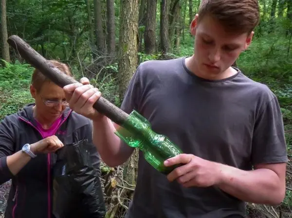 Person hält einen Stock mit einer grünen Plastikflasche im Wald