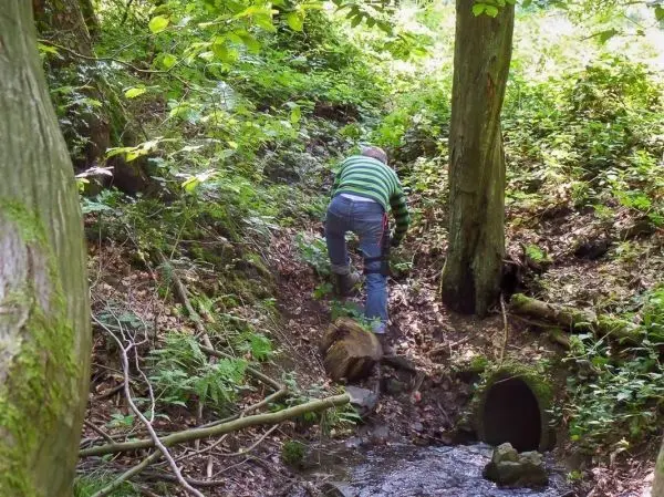 Person klettert an einem steilen Hang neben einem kleinen Bach