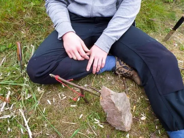 Person sitzt im Gras und hält einen Stock in der Hand