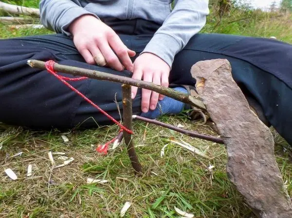 Schlagfalle (Figure-Four) mit Holzstück und Stein auf dem Boden
