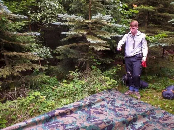 Tarp-Notunterkunft liegt auf dem Boden, Person richtet Ausrüstung aus