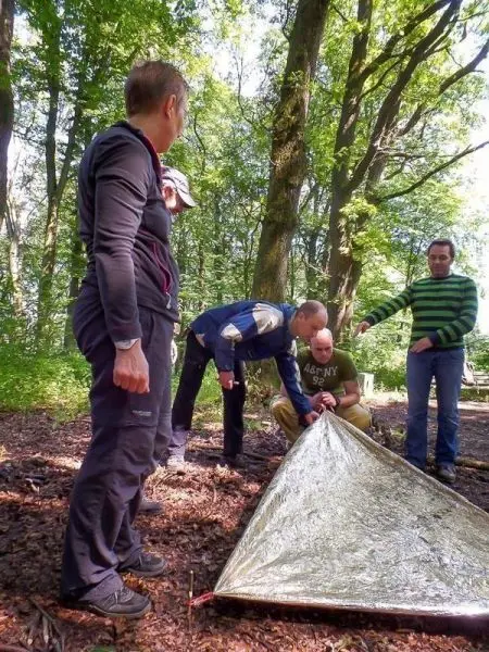 Tarp-Notunterkunft wird von mehreren Personen aufgebaut und gesichert