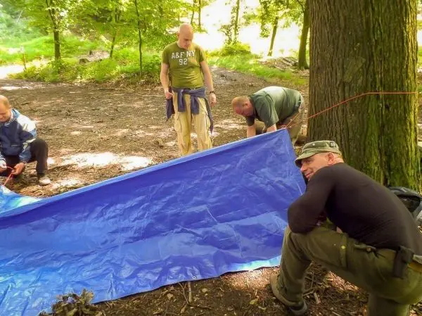 Tarp-Notunterkunft wird von mehreren Personen zwischen Bäumen gespannt