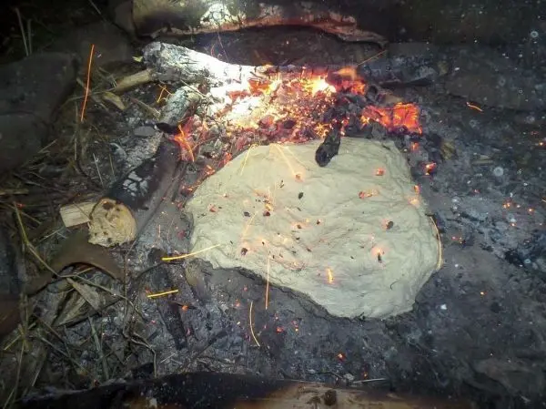 Teigstück liegt auf glühenden Kohlen eines kleinen Bodenfeuers