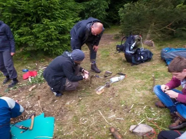 Zwei Personen arbeiten am Boden mit Werkzeugen, während andere im Hintergrund stehen
