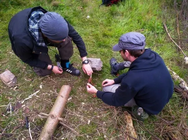 Zwei Personen bereiten Zunder aus Holzstücken auf dem Boden vor