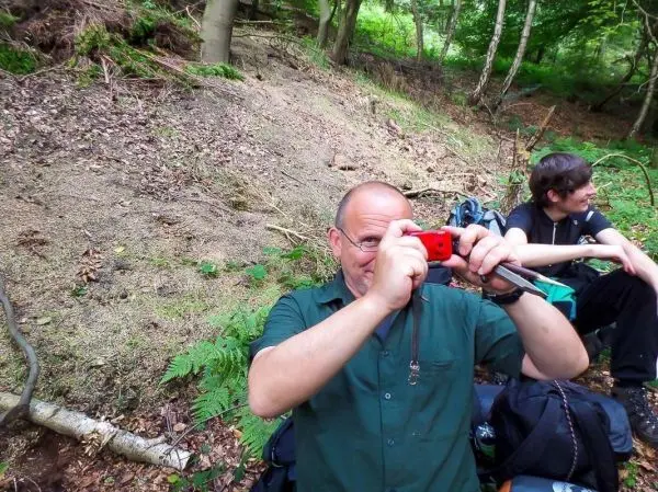 Zwei Personen sitzen im Wald, eine Person hält eine Kamera in der Hand