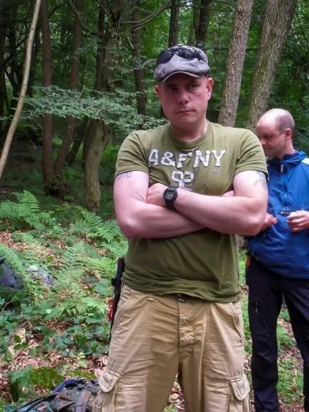 Zwei Personen stehen im Wald zwischen Bäumen und Farnen