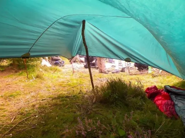 Blick unter einem grünen Tarp auf den Boden und Personen im Hintergrund beim Überlebenstraining