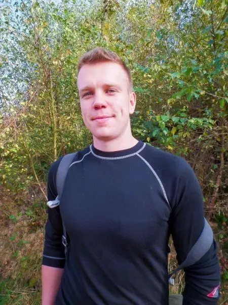 Ein junger Mann steht vor einer grünen, bewaldeten Kulisse