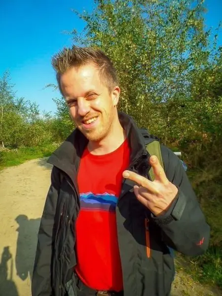 Ein Mann zeigt das Peace-Zeichen und lächelt auf einem Waldweg