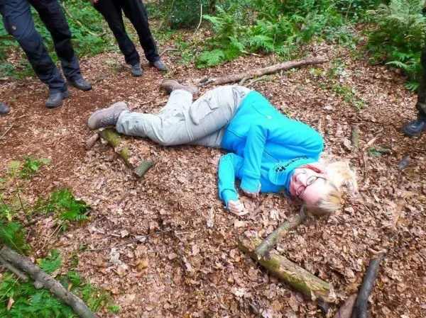 Frau liegt auf dem Boden im Wald, umgeben von Laub und Ästen