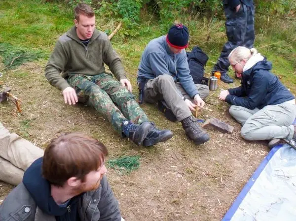 Gruppe arbeitet am Boden mit Holz und Werkzeugen zur Herstellung von Zunder
